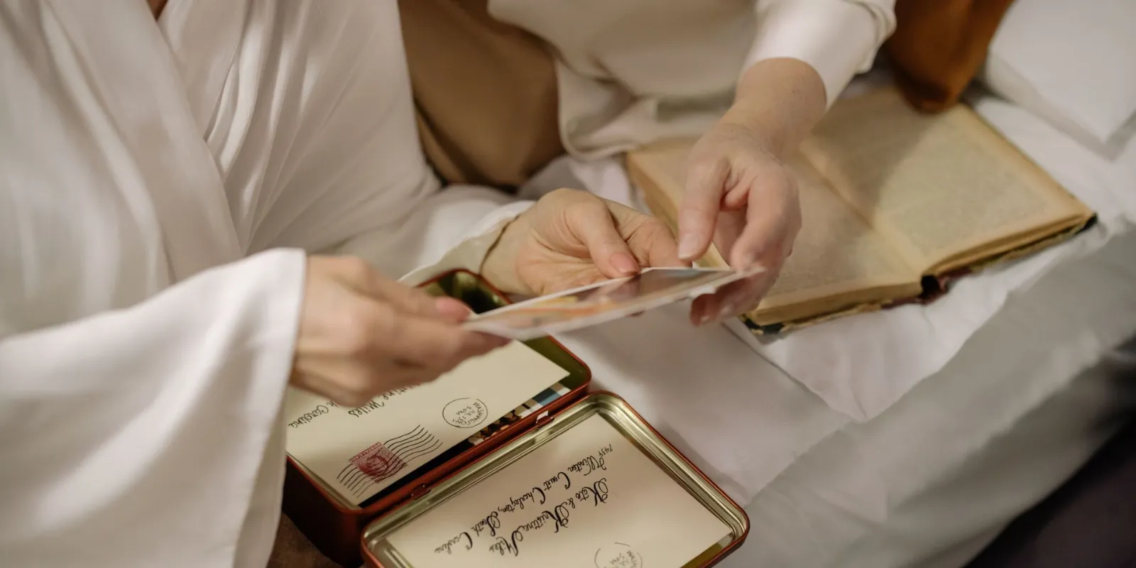 A woman sitting on a bed holding a piece of paper while sorting belongings